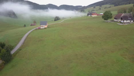 Morning-fog-hangs-low-in-quaint-green-farming-valley-in-Europe,-aerial