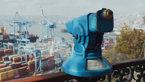 Pan-right-of-an-old-telescope-touristic-viewfinder-pointing-at-Valparaiso-Sea-Port-cranes-and-containers,-Chile