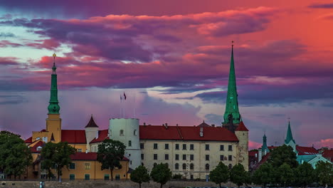 Schöner-Blick-Auf-Die-Altstadt-Von-Riga,-Lettland-Mit-Der-Lettischen-Flagge,-Die-An-Der-Kuppelkathedrale-Weht,-Und-Wolken,-Die-Im-Zeitraffer-Vorbeiziehen