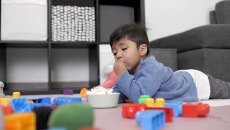 Zwei-Jahre-Alter-Mexikanischer-Junge,-Der-Corn-Pop-Isst,-Auf-Dem-Boden-Liegt-Und-Fernsieht