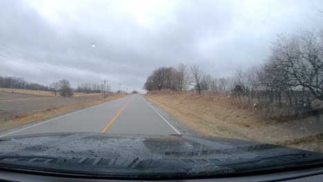 POV-thru-the-windshield-and-active-windshield-wipers-during-a-light-rain-while-driving-on-a-county-road-in-rural-Illinois