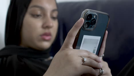 Vista-Borrosa-De-Mujeres-Musulmanas-Jóvenes-Que-Usan-Hiyab-Escribiendo-En-Un-Teléfono-Inteligente-Mientras-Se-Sientan-En-El-Sofá