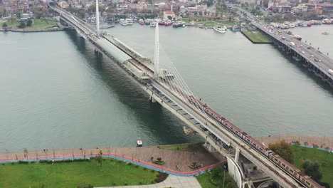 Drone-Aéreo-Que-Rodea-El-Puente-Del-Metro-Halic-Mientras-Un-Tren-Cruza-El-Río-Bósforo-Durante-Una-Mañana-Nublada-En-Estambul,-Turquía