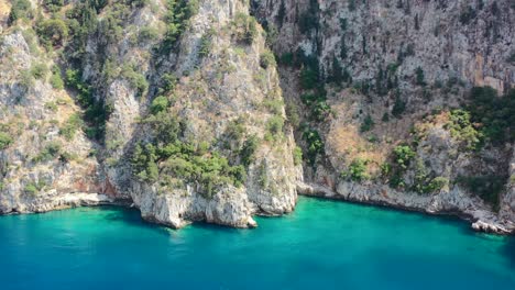 aerial-drone-approaching-a-beautiful-turquoise-blue-ocean-bay-near-Butterfly-Valley-in-Fethiye-Turkey-surrounded-with-green-mountain-cliffs-on-a-sunny-summer-day