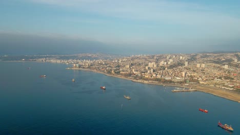 Aerial-dolly-in-of-Valparaiso-picturesque-hillside-city-and-cargo-ships-sailing-in-sea-near-the-coastline,-Chile