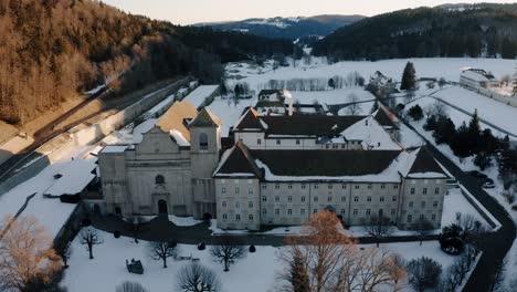 The-abbey-of-Bellelay,-historical-monument-of-the-Bernese-Jura-in-Switzerland,-aerial-shot-by-drone-during-sunrise