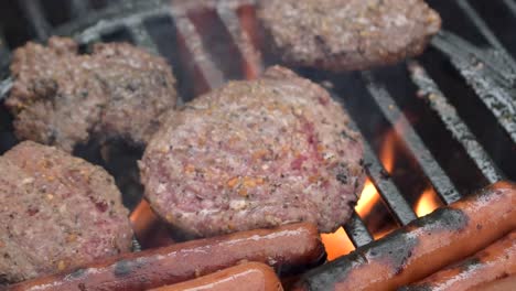 outdoor-grill-closeup-of-seasoned-beef-hamburger-patties-and-hot-dogs-cook-over-flames-with-smoke