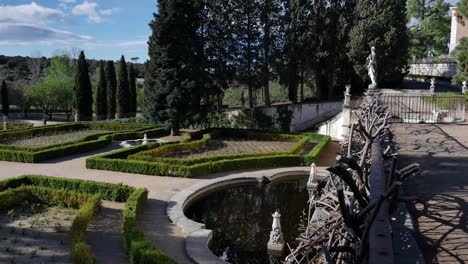 Panning-to-the-left-general-shot-of-a-baroque-garden,-with-fountains,-and-a-fence-with-dead-branches-in-the-right-at-the-beginning