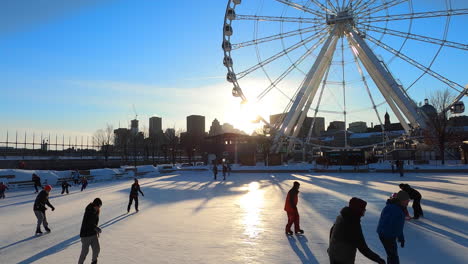 Ice-Skating-Rink-in-Old-Port-Montreal-next-to-Big-Ferris-Wheel,-People-Skaters-Enjoying-Outside-Winter-Skate-Activities-Leisure,-Winter-Tourist-Attraction-Destination,-Montreal-Buildings-in-Background