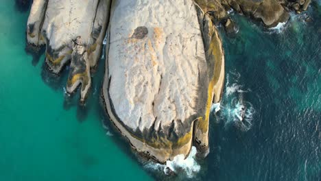 blue-ocean-waves-crashing-on-large-boulders-at-Llandudno-Beach-in-Cape-Town,-top-down-aerial