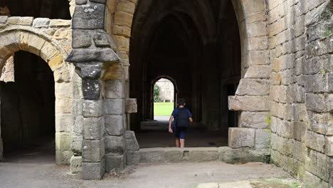 Joven-Caminando-A-Través-De-Un-Arco-Medieval-En-Las-Ruinas-De-La-Abadía-De-Fountains-En-Yorkshire,-Reino-Unido