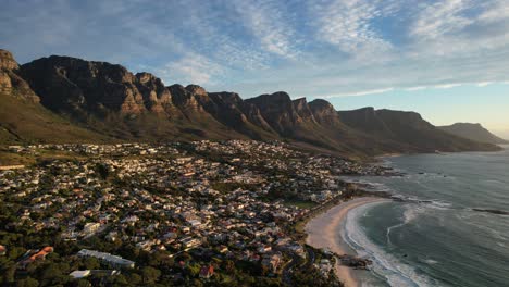 Camps-Bay-beach-coastline-at-sunset-with-twelve-apostles-in-background,-aerial