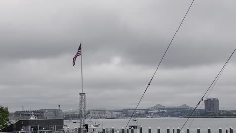 America-flag-waving-in-the-wind-in-the-Boston-harbor-on-a-cloudy,-overcast-summer-day