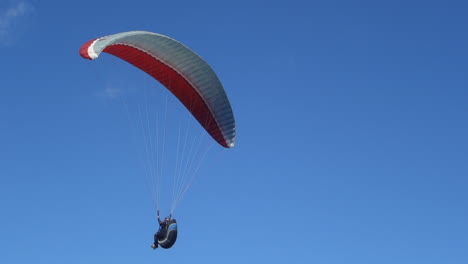 Paraglider-below-a-red-and-white-canopy-flies-close-against-blue-sky