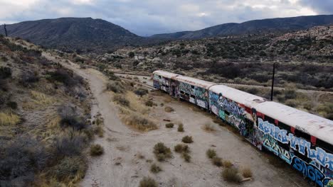 Aerial-view-passing-a-abandoned-train-in-middle-of-cloudy-desert---tilt,-drone-shot