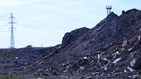 Exterior-view-of-abandoned-Soviet-heavy-metallurgy-melting-factory-Liepajas-Metalurgs-territory,-piles-of-debris-and-junk,-distant-electrical-powerlines,-sunny-day,-wide-shot