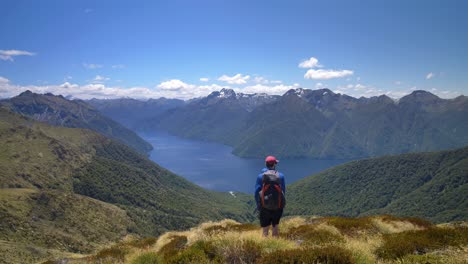 Static,-hiker-overlooks-landscape-of-lake-surrounded-by-mountains,-Kepler-Track-New-Zealand