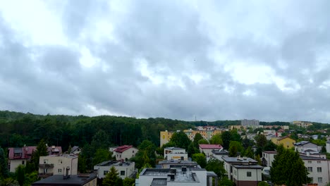 Time-lapse-shot-of-grey-clouds-flying-over-rural-town-with-colorful-houses-beside-forest-trees