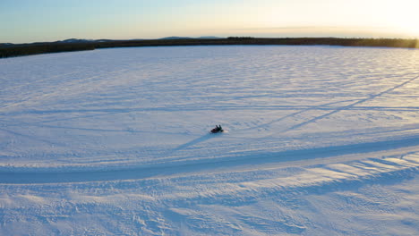 Aerial-view-single-snowmobile-driver-travelling-fast-across-vast-snowy-Nordic-winter-wilderness-away-from-sunrise