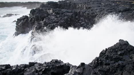White-foam-wave-splashing-through-black-basalt-rock-shore,-Iceland,-slow-motion