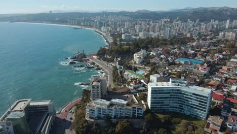 Aerial-dolly-in-of-luxurious-resorts-and-city-and-buildings-near-turquoise-sea,-hills-in-background,-Viña-del-Mar,-Chile