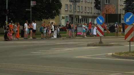 FIA-European-Rally-Trophy-2022-festive-start-and-cars-parade-at-streets-of-Liepaja-,-golden-hour-evening,-rally-cars-passing-spectators,-medium-angle-handheld-tracking-shot