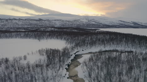 Aerial-view-above-dramatic-Scandinavian-sunrise-mountains-with-scenic-snow-covered-woodland-lake-wilderness