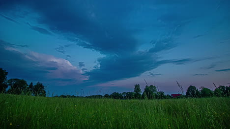 Cumulus-clouds-billow-above-the-grassy-meadow-and-trees-at-sunset-in-the-tranquil-countryside---time-lapse