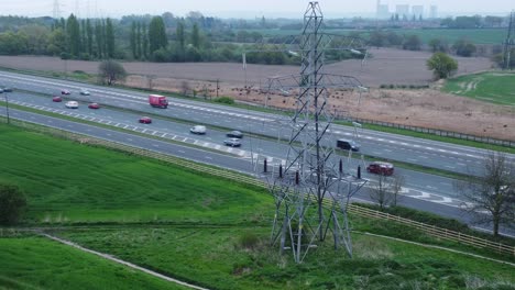 Vehicles-on-M62-motorway-passing-pylon-tower-on-countryside-farmland-fields-aerial-view-wide-left-orbit