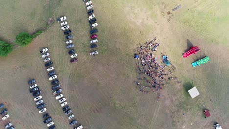 Top-down-shot-of-crowd-of-gathering-for-a-baptism-with-cars-parked-in-the-field