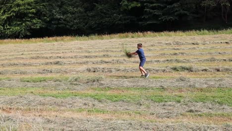 Young-boy-throwing-grass,-hay-into-the-air-in-a-freshly-cut-field