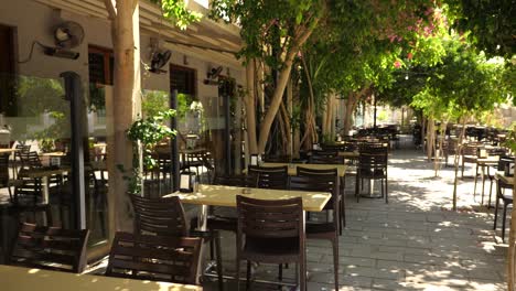 Vista-De-Una-Cena-Vacía-Al-Aire-Libre-En-Una-Calle-Sombreada-En-Nicosia-Con-Hombres-Saliendo-Y-Caminando