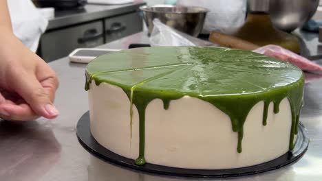 Rear-shot-of-a-professional-french-pastry-chef-using-serrated-knife-to-slice-moist-japanese-matcha-green-tea-sponge-cake-with-delicious-buttercream-meringue,-portioning-in-precision