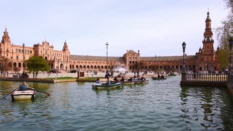Tourist-in-rowing-boats-in-the-water-canals-in-front-of-the-impressive-architecture-at-Plaza-de-Espana-Seville,-Spain
