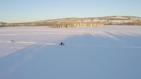 Aerial-view-tracking-three-snowmobiles-riding-across-snowy-Lapland-Nordic-wilderness-trail