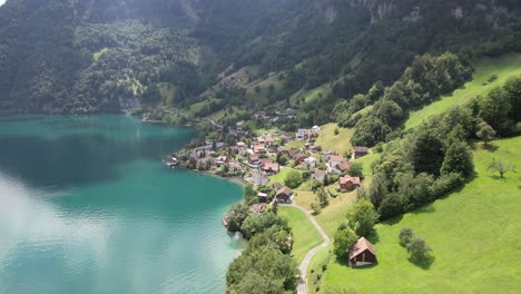 Blauer-See-Und-Kleines-Schweizer-Dorf-Mit-Drohnenblick-Auf-Berge-Und-Natur
