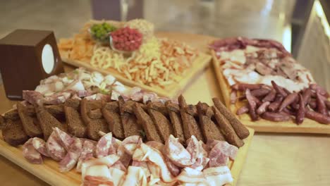 Three-wooden-boards-with-bread,-fat,-smoked-meat-and-cheese,-three-glasses-of-flavoured-and-original-peanuts,-sausages-and-chips