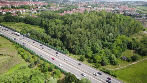 Aerial-Tilt-View-of-Fluid-Cars-and-trucks-Traffic-on-Multi-Lanes-Countryside-Highway-in-Gdynia-Area-Poland,-Surrounded-by-Fields-Green-Lands-Trees-and-Suburban-Homes-in-Horizon,-Travel-and-Transport