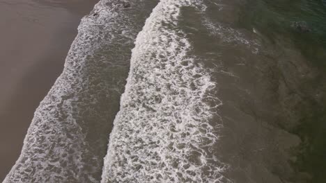 Luftaufnahme-Der-Schäumenden-Wellen-Des-Pazifischen-Ozeans,-Die-Auf-Den-Sandstrand-Treffen