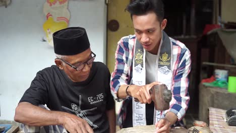 Elderly-Old-man-is-showing-how-to-create-shadow-Puppets-or-wayang-kulit-using-hammer-and-nails-to-the-young-man-beside-him-or-Putera-Pariwisata-Jawa-Barat
