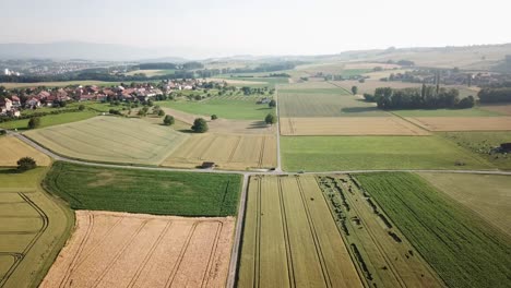 High-drone-aerial-view-of-the-swiss-countryside,-different-fields:-wheat,-vegetables-and-a-small-village,-Vaud
