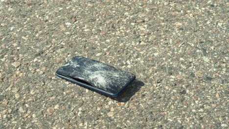 Vehicle-tire-runs-over-modern-smart-phone-on-paved-road,-destroying-it