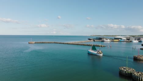 An-aerial-view-A-small-fishing-boat-sails-through-the-harbor-gate-to-the-open-sea-on-a-sunny-evening
