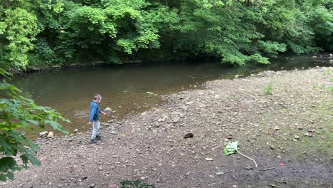 Young-boy-throwing-stones-into-a-woodland-river-and-having-fun