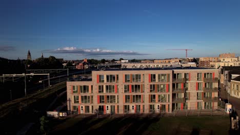 Aerial-backwards-reveal-of-wider-park-and-Noorderhaven-neighbourhood-at-sunrise-with-the-Ubuntupplein-apartment-building-lit-up-brightly-and-colorful-against-a-vibrant-blue-sky