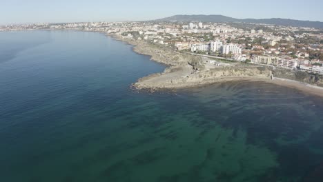 Aerial-drone-view-of-Sao-Pedro-do-Estoril-Beach-in-Sao-Pedro-do-Estoril,-Greater-Lisbon,-Cascais-in-background
