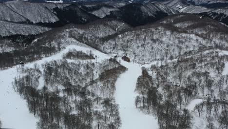 snow-capped-mountain-peaks-with-skiers-in-winter-at-nozawa-japan-in-nagano-region,-aerial
