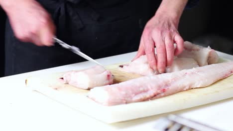 A-fishmonger-cleaning-up-a-hake-fish,-making-it-portions-for-the-restaurant