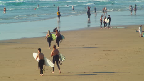 Surfistas-Caminando-En-La-Playa-Soleada-Entre-Otros-Vacacionistas-En-Perranporth,-Cornualles,-Inglaterra