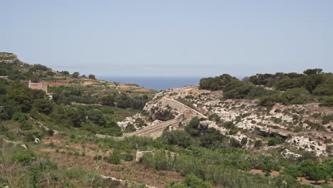 Paisaje-Rural-De-4k-Con-Una-Antigua-Muralla-Y-El-Mar-Mediterráneo-A-Lo-Lejos-En-La-Isla-De-Malta-Durante-Un-Caluroso-Día-De-Verano
